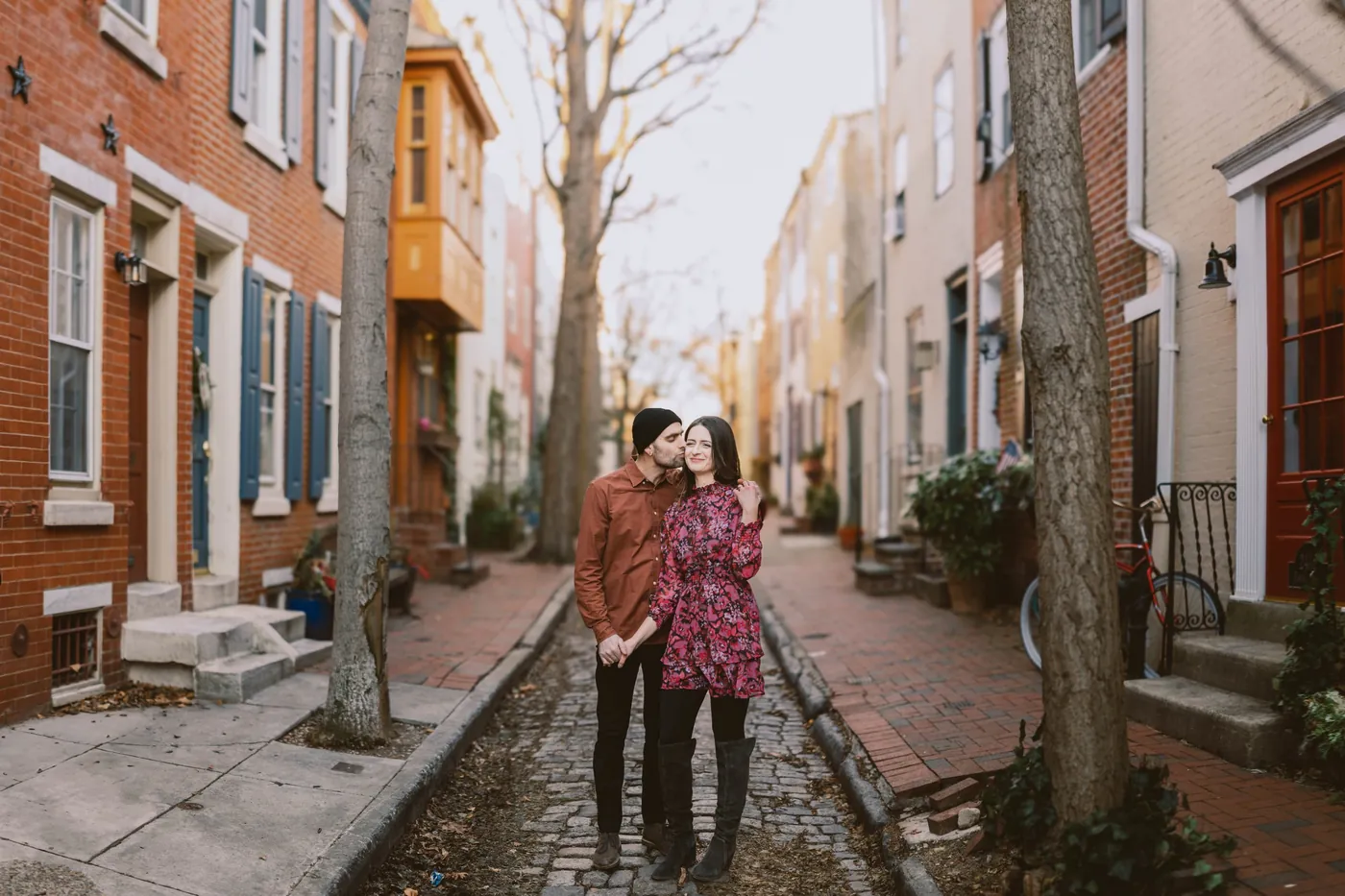 Engaged couple sharing a kiss on a cobblestone street lined with brick rowhouses in Old City, Philadelphia