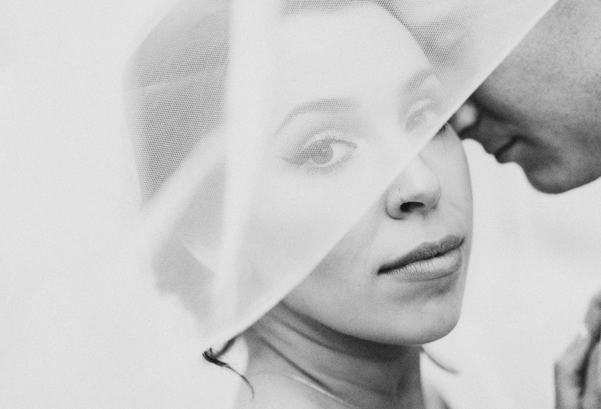 Black and white close-up of a bride looking through her veil as the groom leans in
