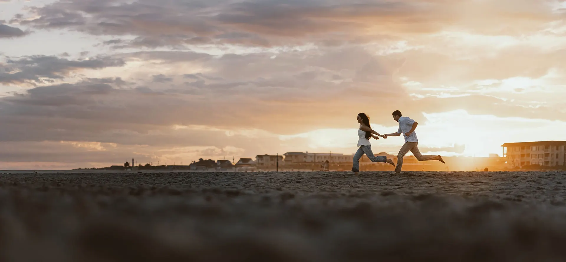 Engaged couple running hand in hand along the beach at sunset near Congress Hall in Cape May, New Jersey