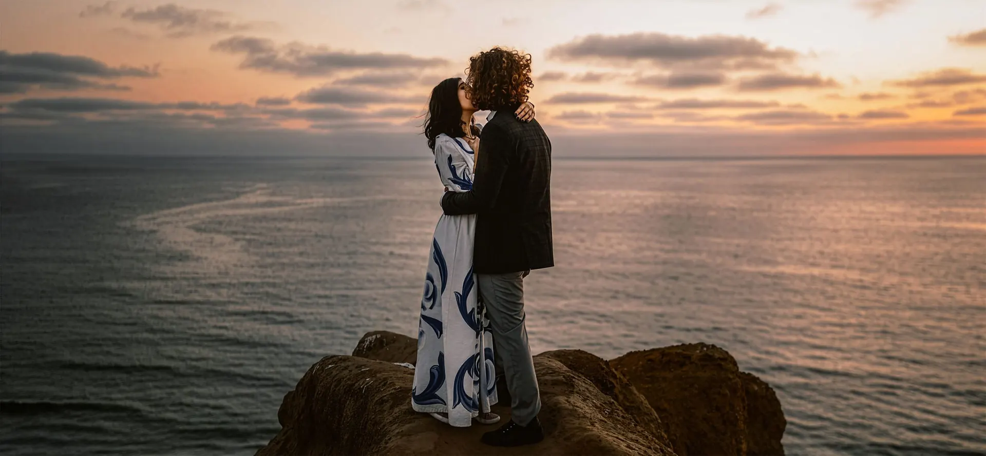 Couple kissing on a rocky cliff above the ocean at sunset in Los Angeles