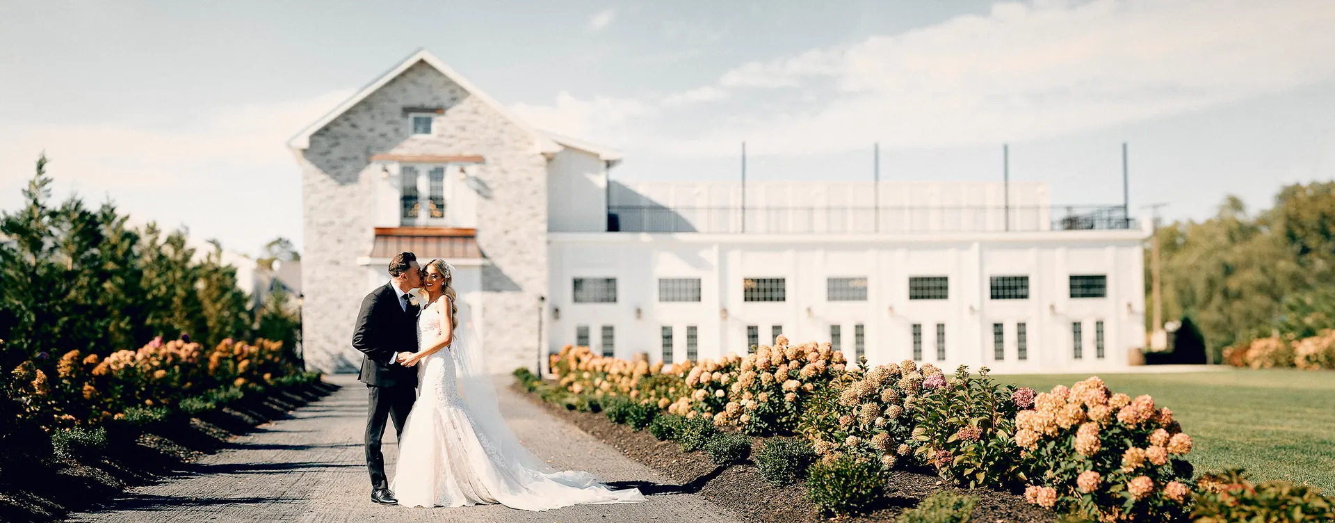 Bride and groom kissing on a hydrangea-lined path at Renault Winery in New Jersey