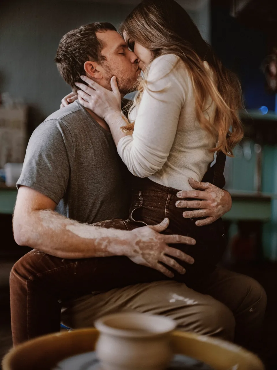 Engaged couple kissing beside a pottery wheel during a pottery class engagement session in Philadelphia