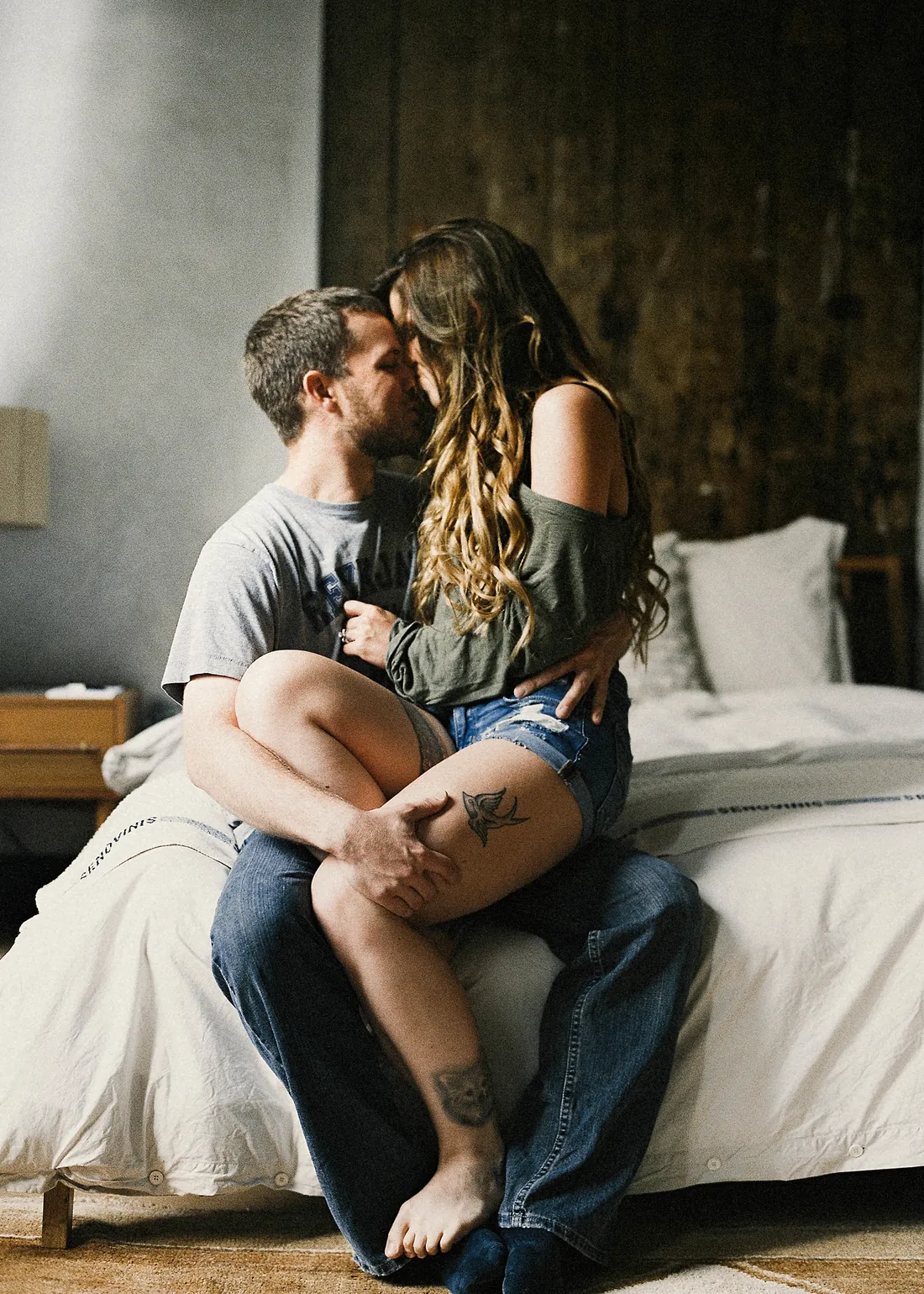 Engaged couple embracing on the edge of a bed at home