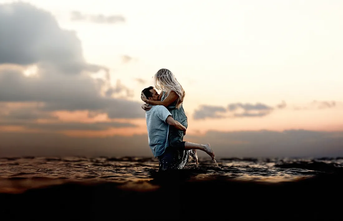 Engaged couple in a lift and kiss in shallow water at sunset