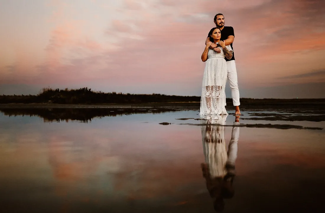 Engaged couple reflected in still water under a pink sky at Barnegat Lighthouse on Long Beach Island, NJ