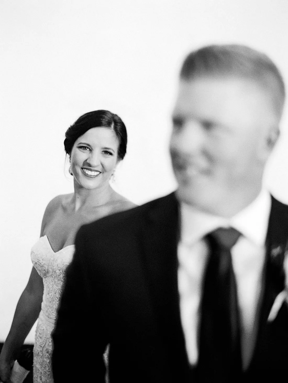 Black and white film photograph of a smiling bride behind her groom