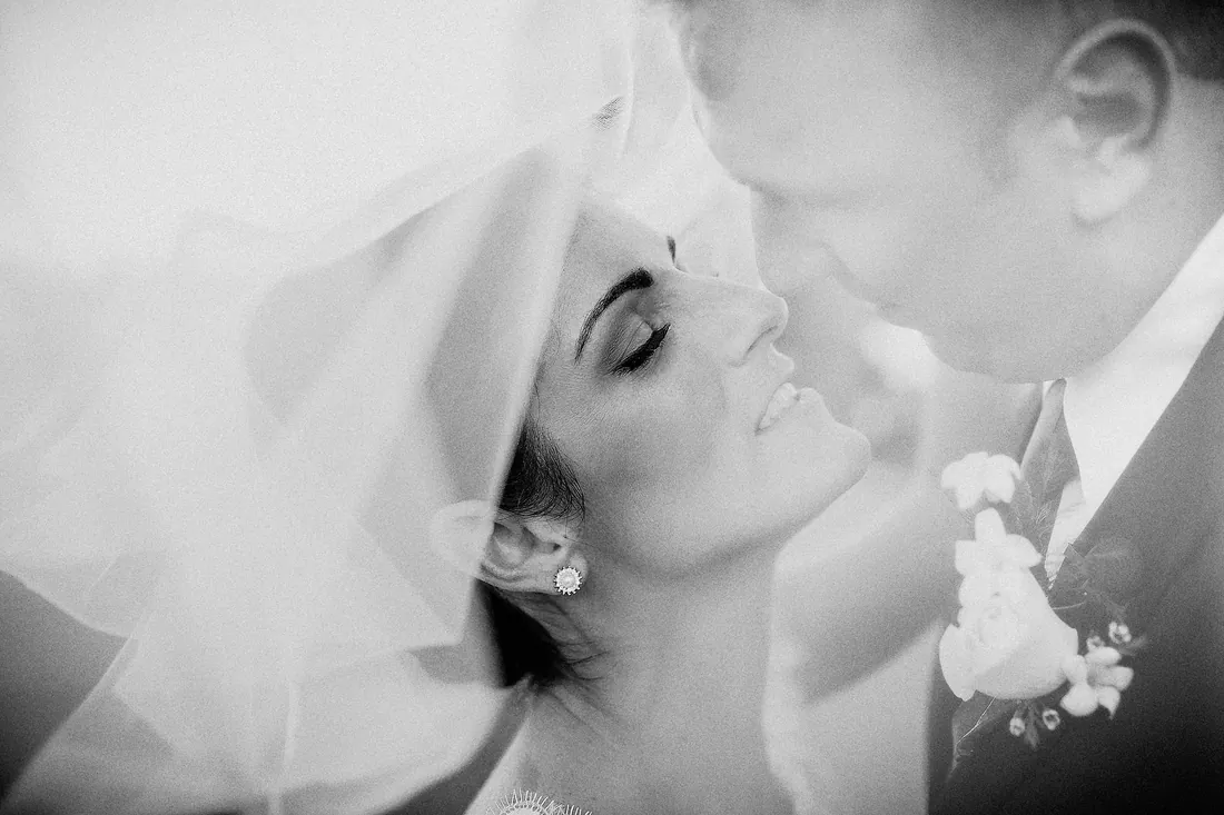 Black and white close-up of a bride and groom about to kiss under her veil