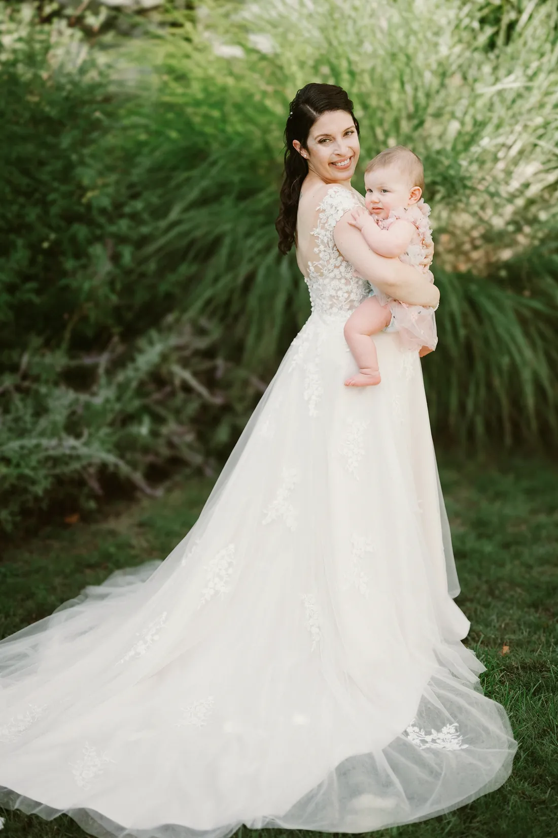 Bride holding a smiling baby in a garden
