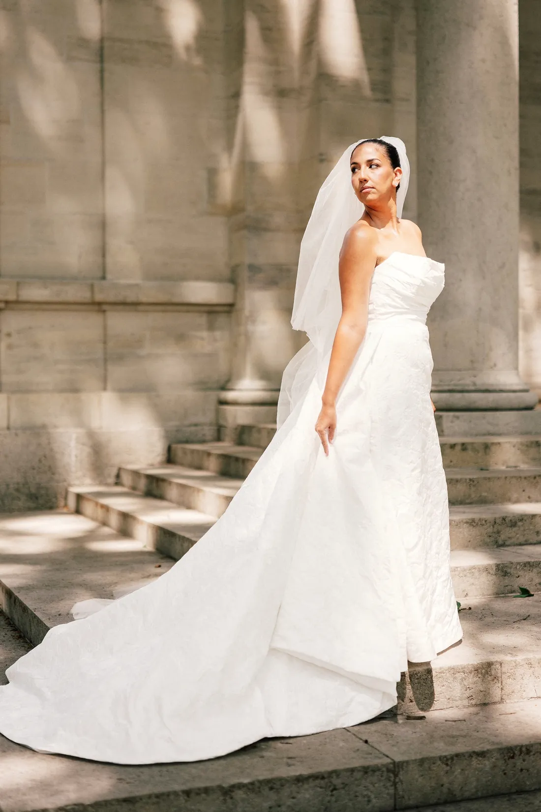 Bride on sunlit stone steps in her gown and veil