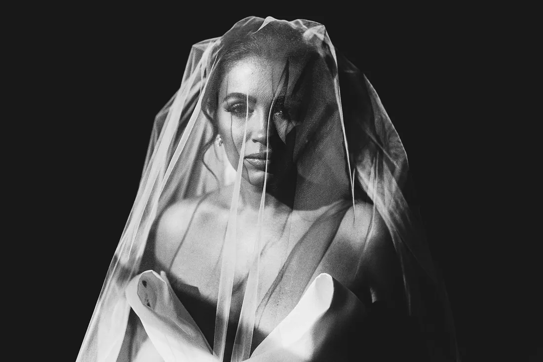 Black and white portrait of a bride in dramatic light under a sheer veil