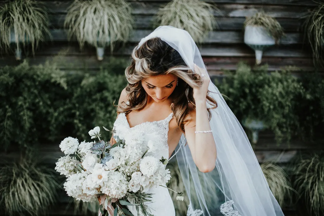 Bride with her bouquet and long veil in front of a living plant wall