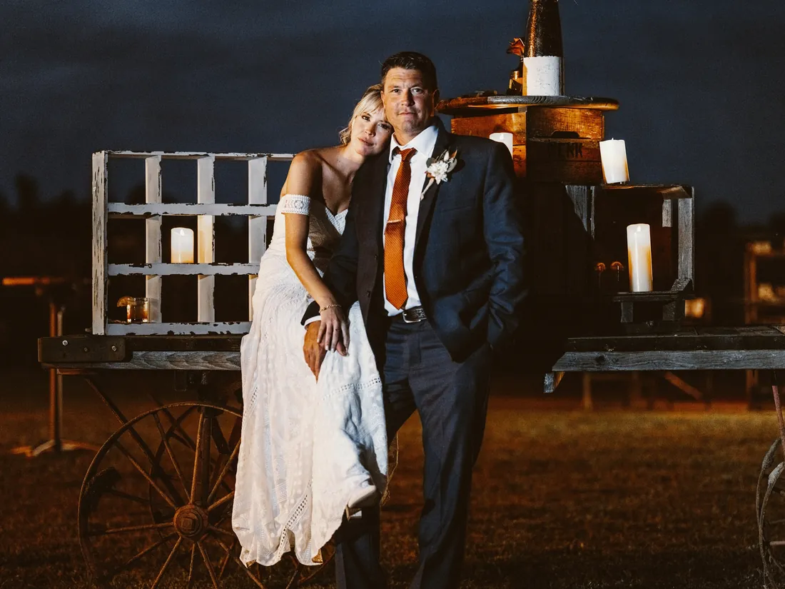 Bride and groom leaning on a candlelit wooden cart at dusk
