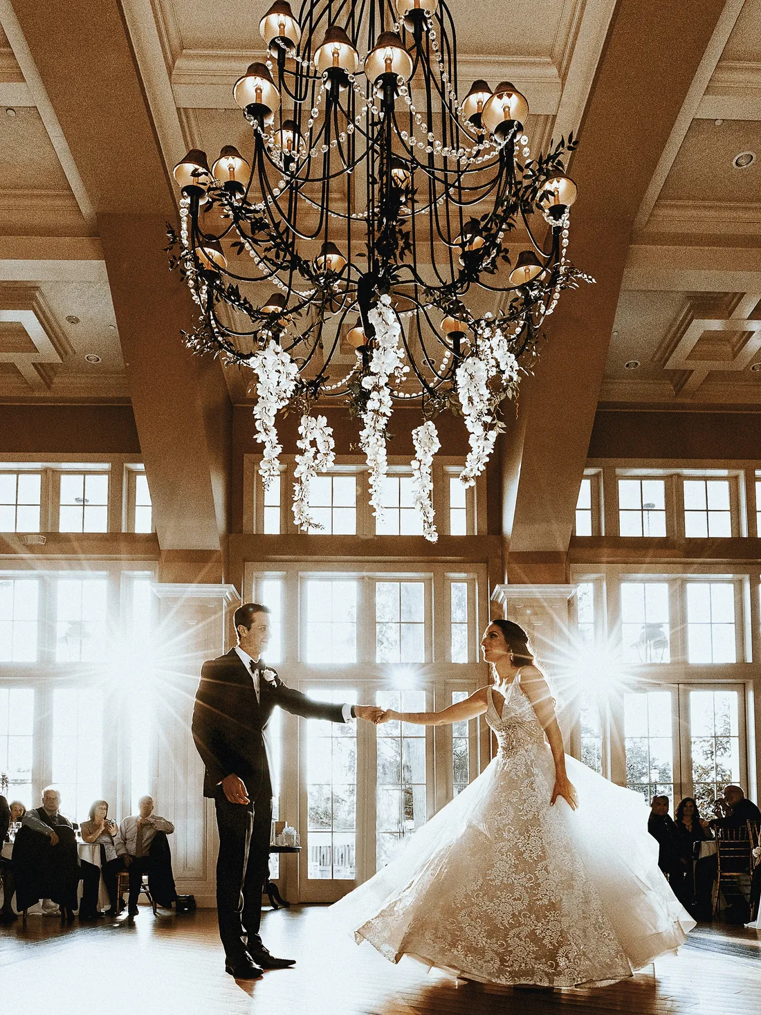 Bride and groom dancing under a grand chandelier as guests watch
