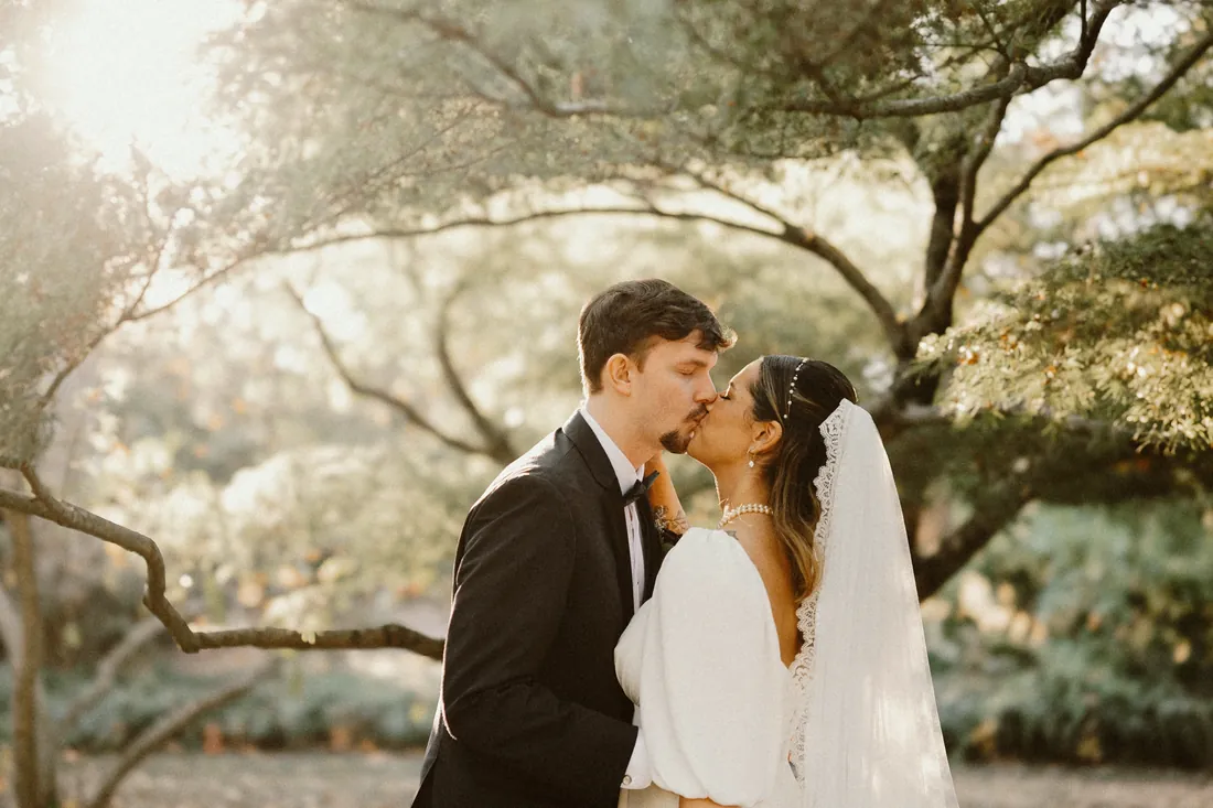Bride and groom kissing under an old tree in soft light
