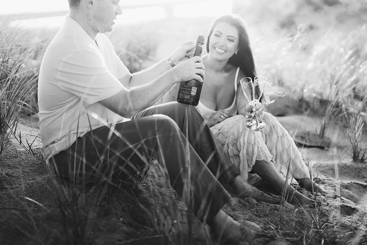 Black and white photo of Branon and Celeste with champagne in the dunes