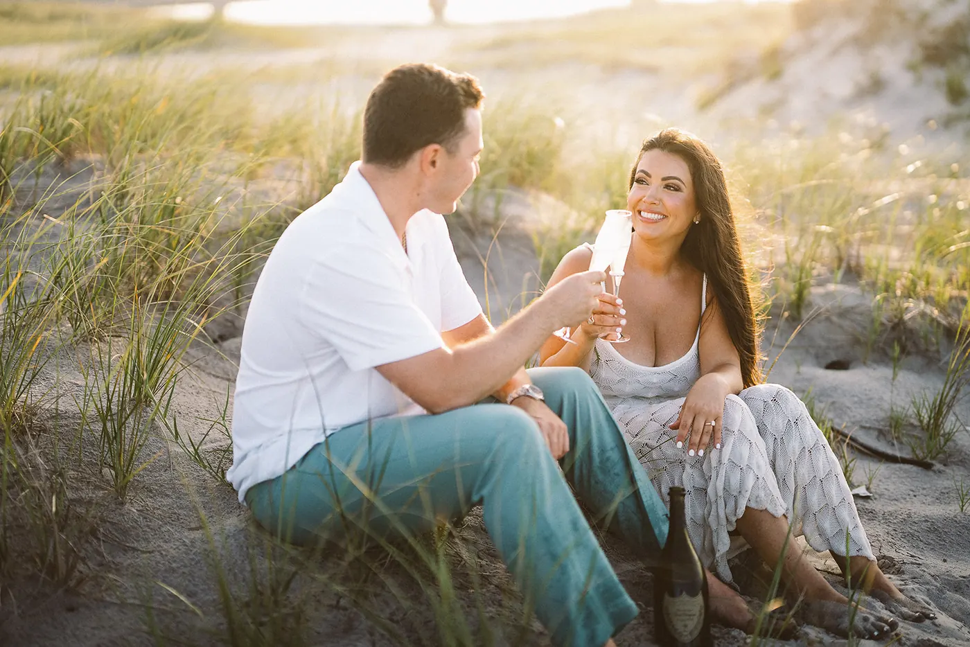 Branon and Celeste toasting with champagne in the dunes at sunset in Ocean City, NJ, near the Longport bridge