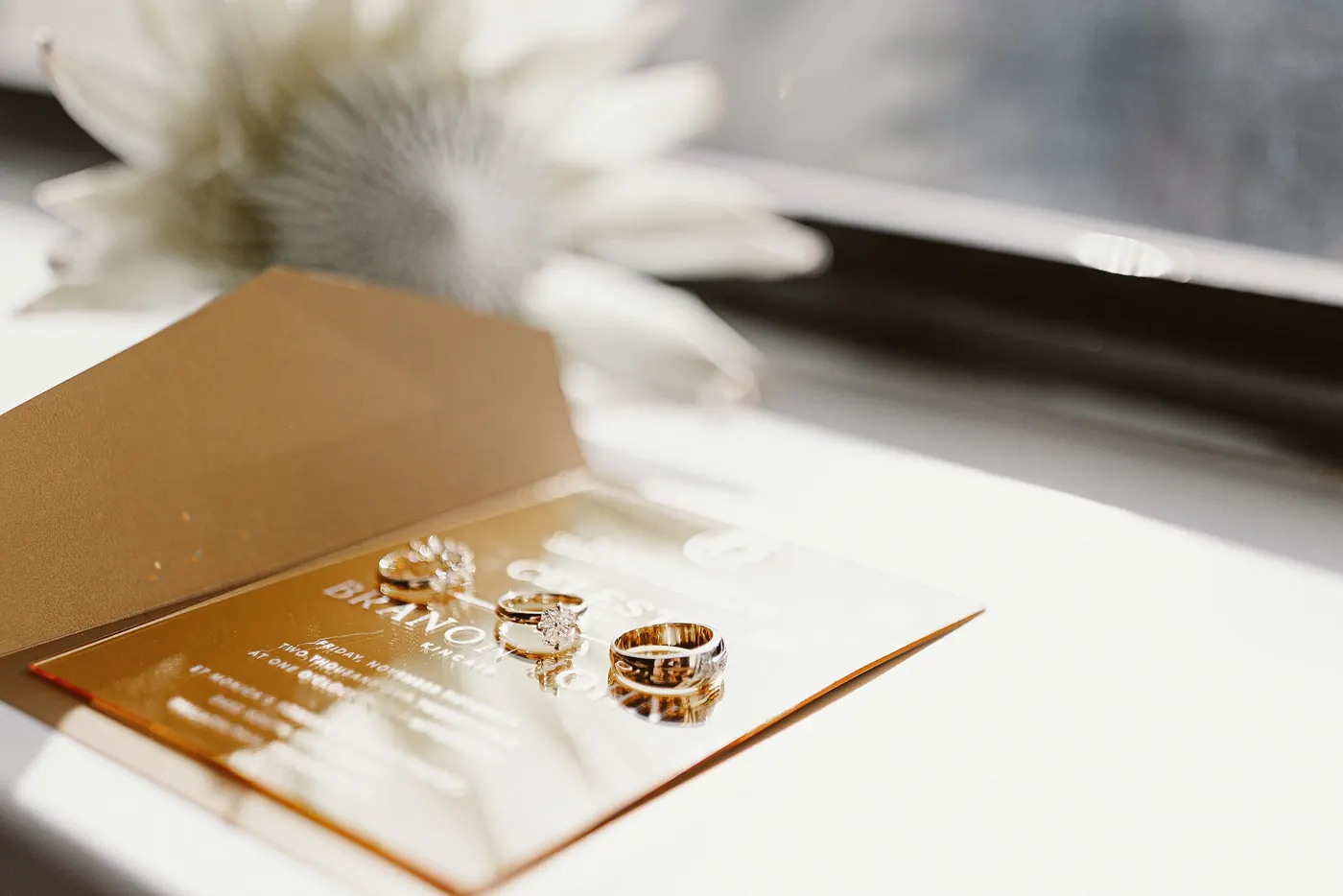 Wedding rings resting on a gold acrylic invitation