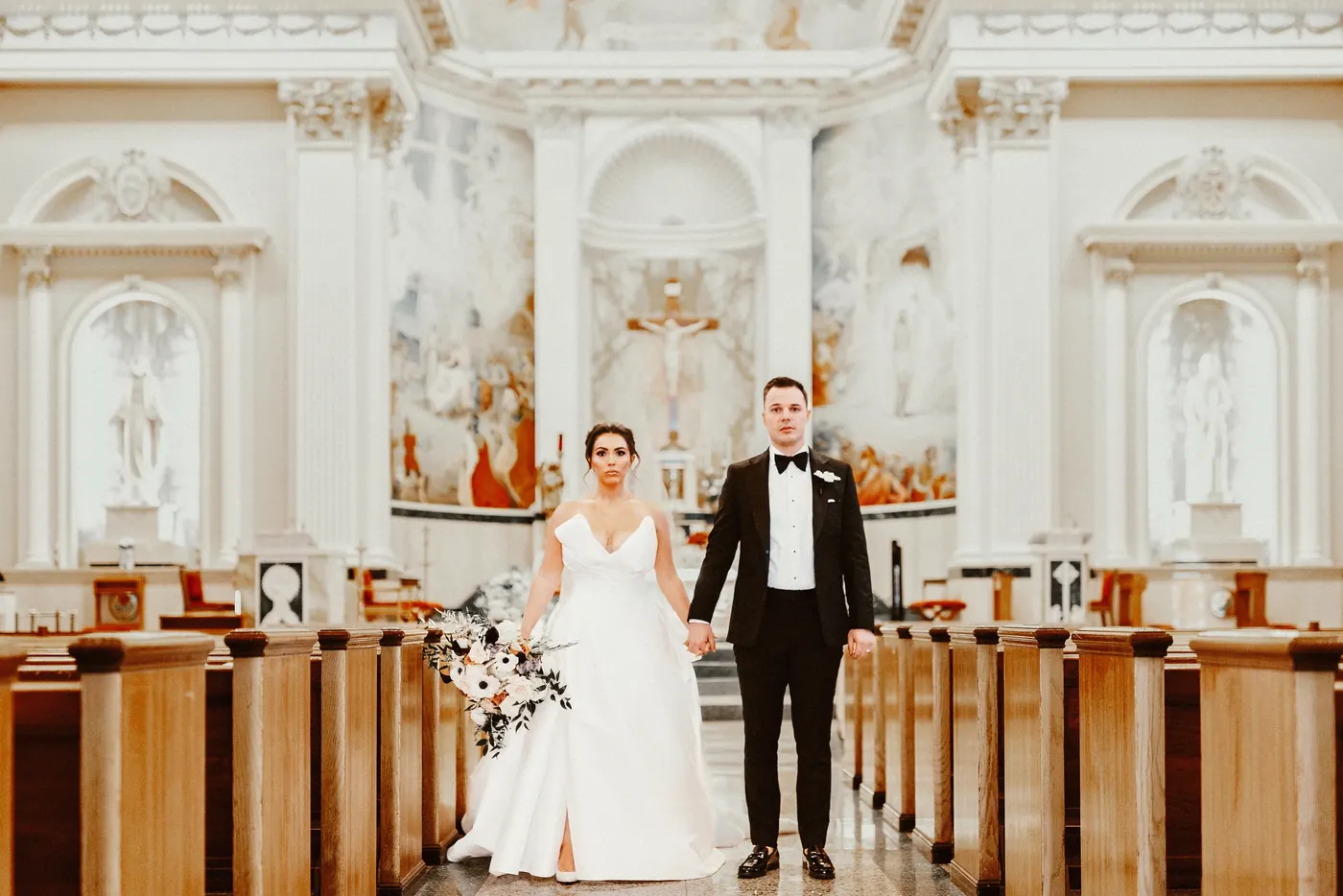 Branon and Celeste standing hand in hand in the aisle of Saint Monica Roman Catholic Church in South Philadelphia after their ceremony