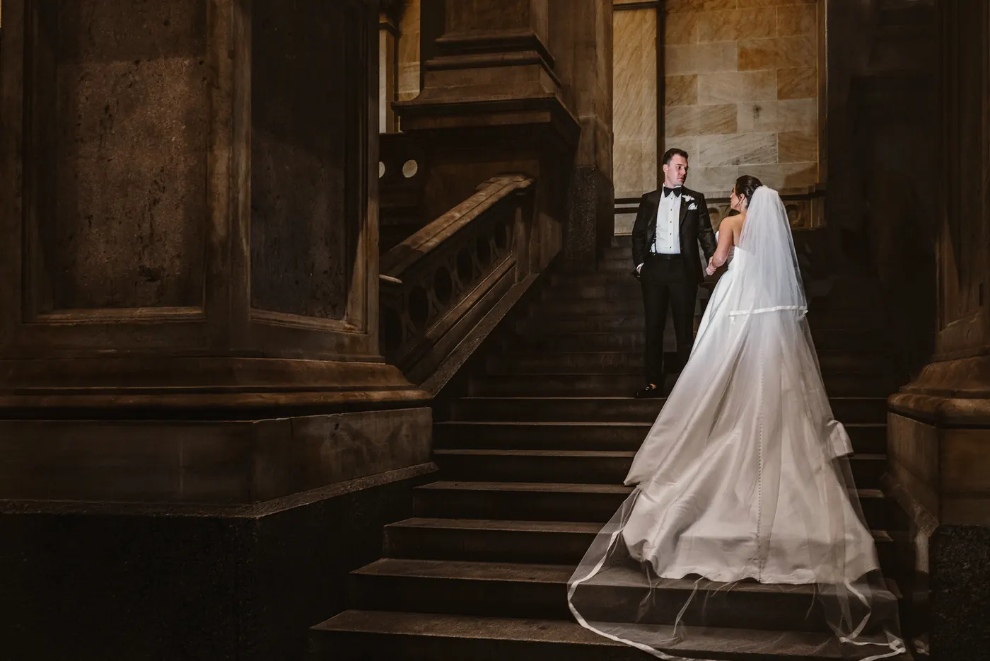 Branon and Celeste on a dark stone staircase with her veil trailing at Philadelphia City Hall