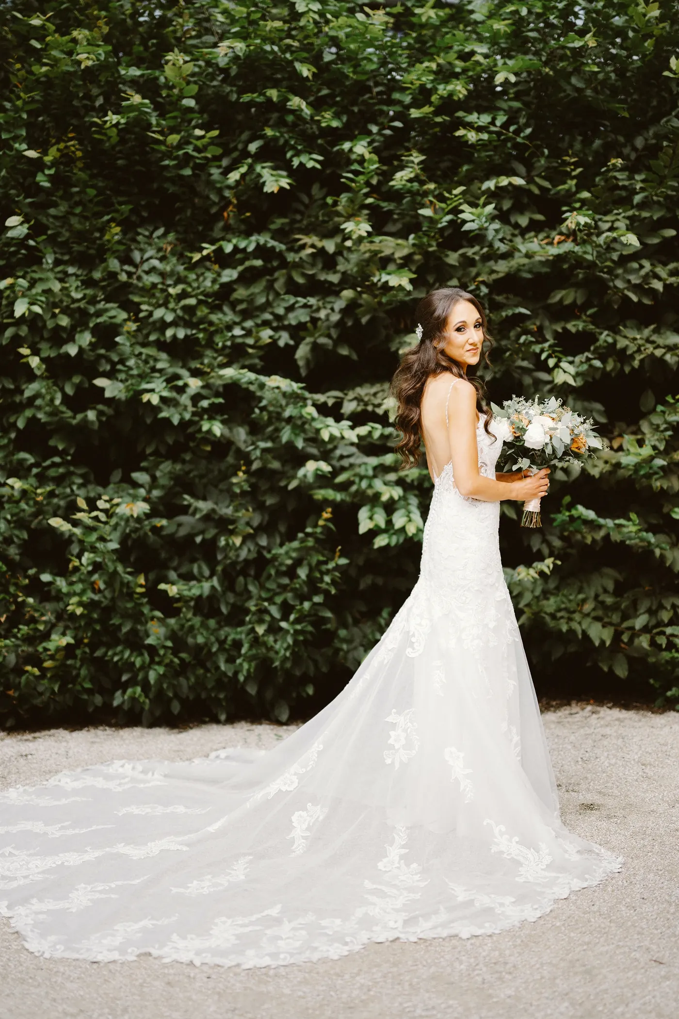 Danielle with her bouquet and long lace train in front of a green hedge at the Rodin Museum in Philadelphia