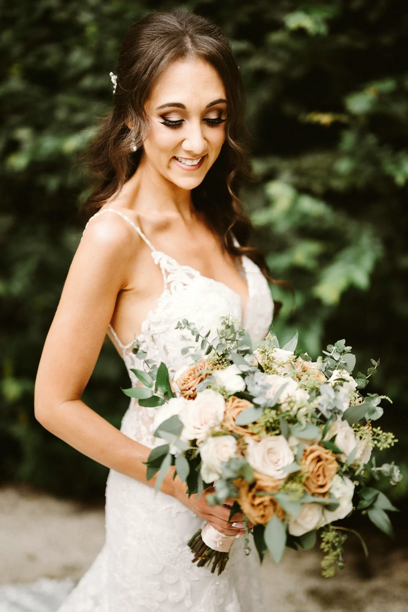 Danielle smiling down at her bouquet of roses and greenery at the Rodin Museum in Philadelphia