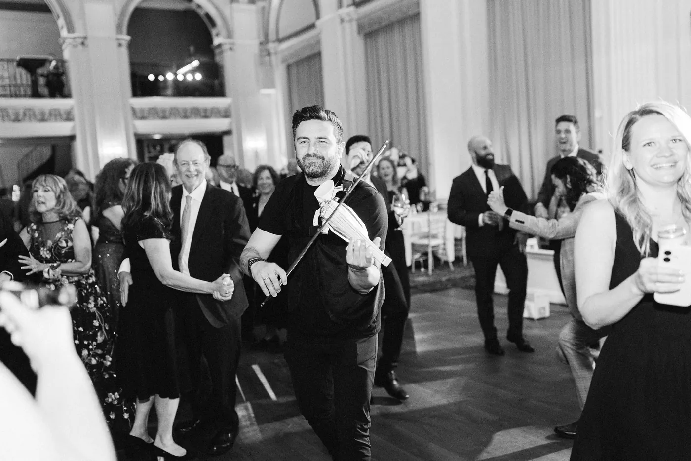Black and white photo of a violinist playing among dancing guests at Cescaphe Ballroom at the Ben in Philadelphia