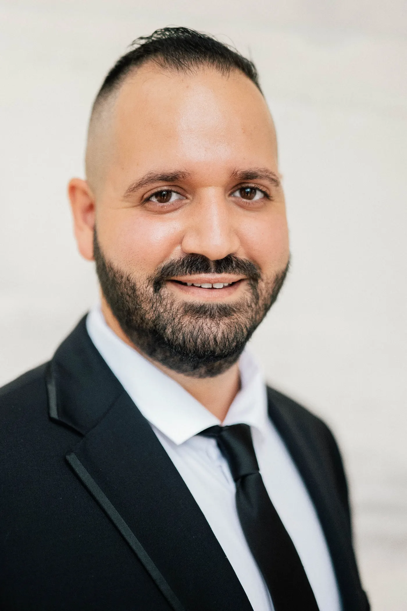 Portrait of Simon smiling in a black suit and tie