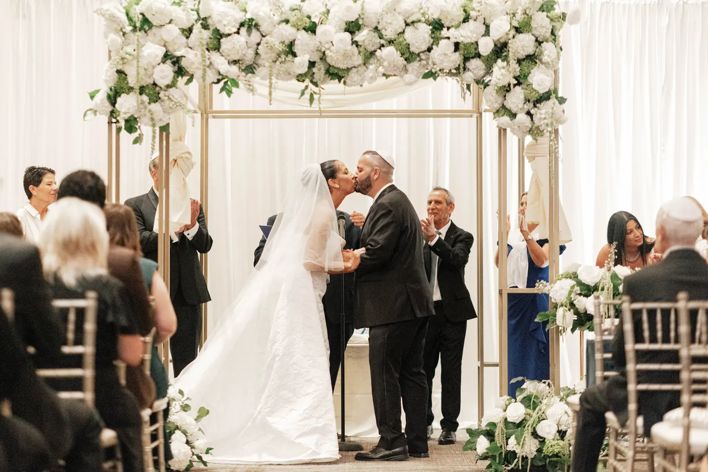 Gianna and Simon's first kiss under a white floral chuppah at the Union Trust