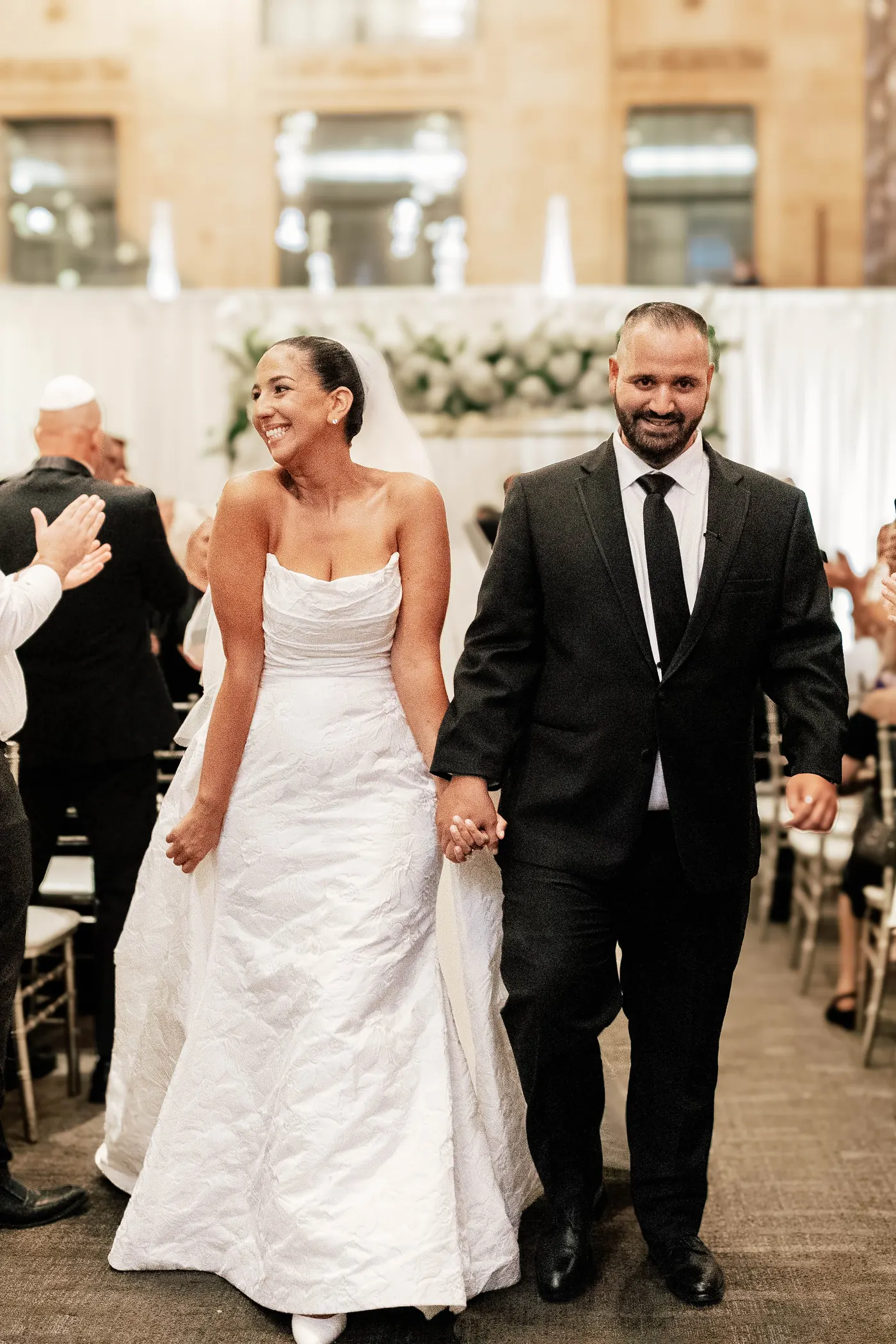 Gianna and Simon smiling and holding hands as they walk up the aisle married