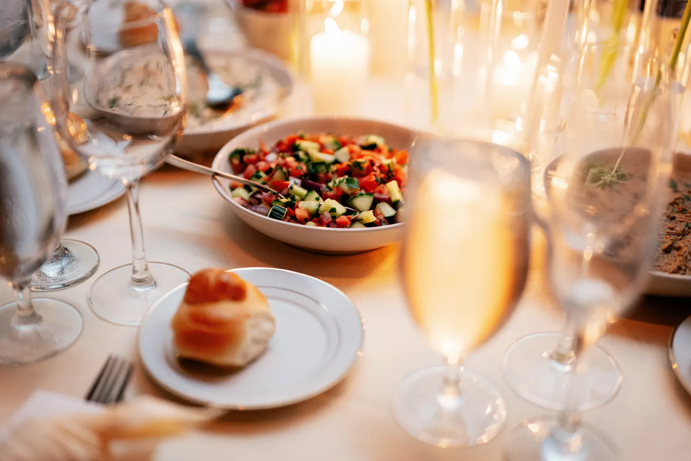 Close-up of a challah roll and a fresh salad by candlelight