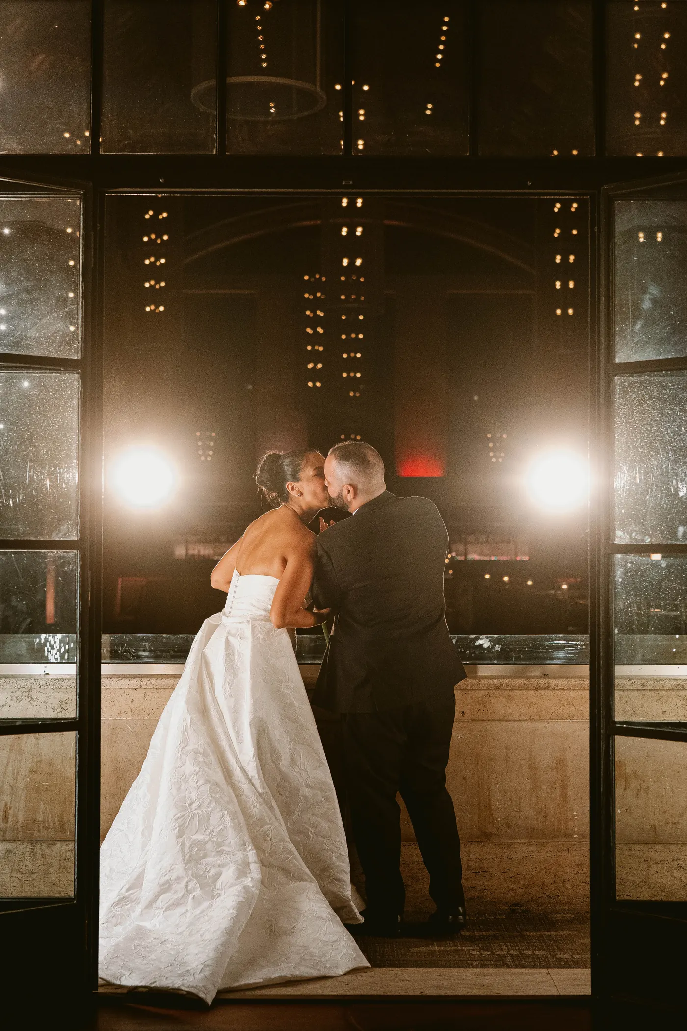 Gianna and Simon sharing a kiss by the tall windows at night