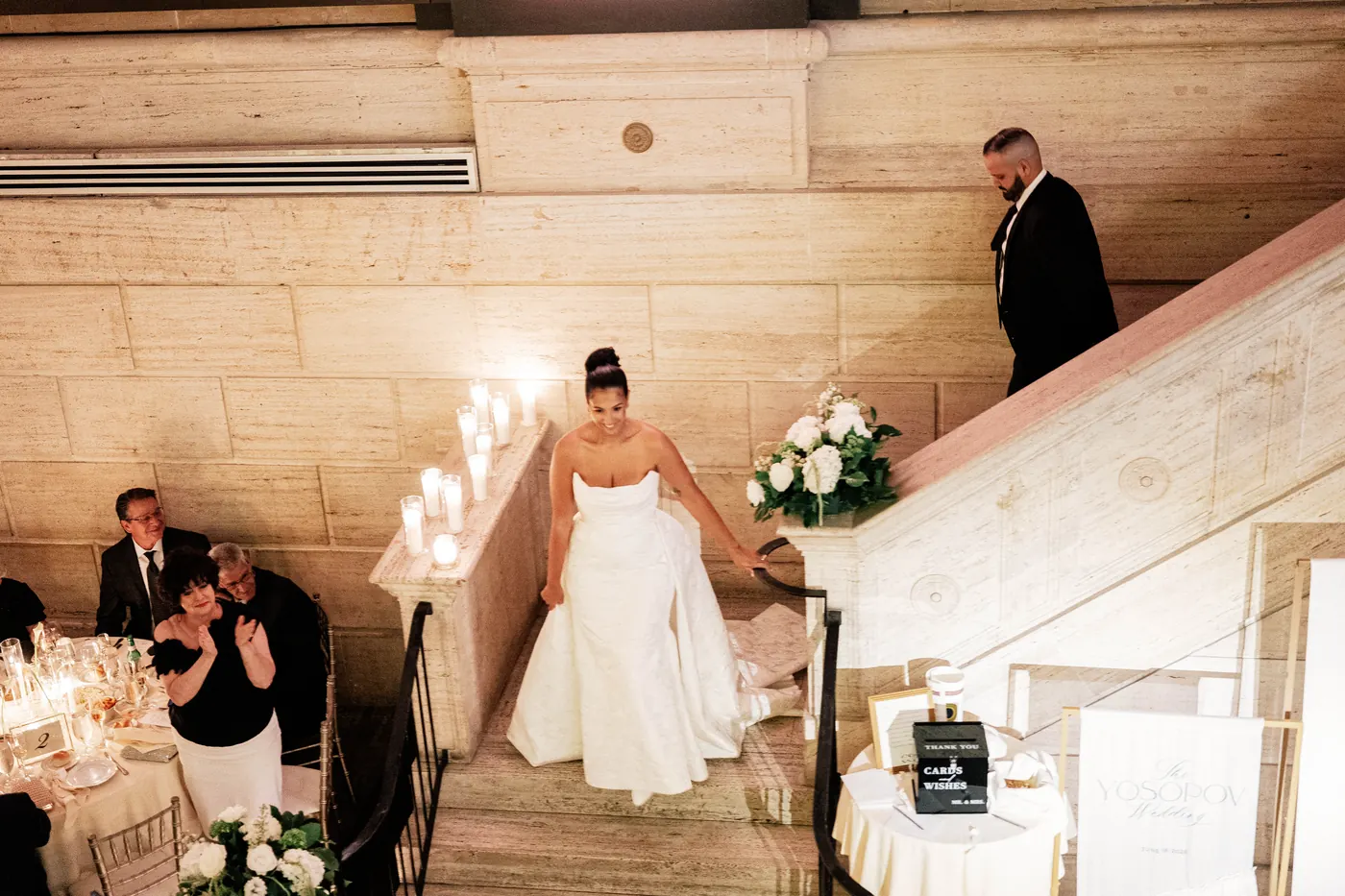 Gianna walking down the candlelit staircase into the reception as guests cheer