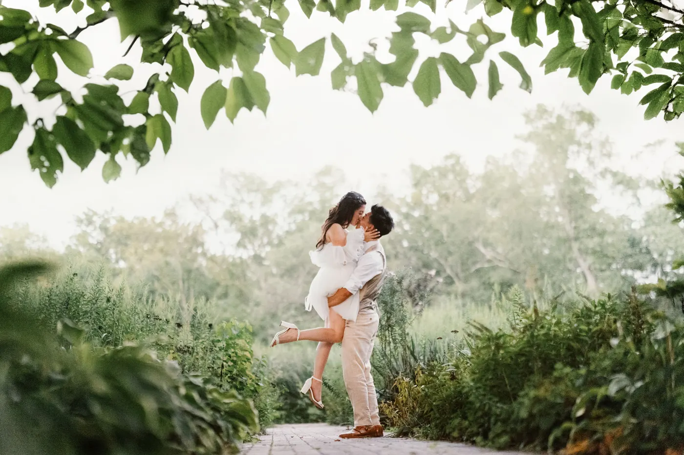 Ivan lifting Camille for a kiss on the garden path, framed by leaves