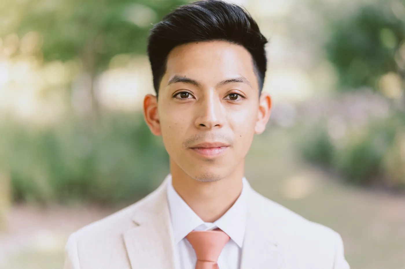 Portrait of Ivan in a tan linen suit and coral tie in the gardens at Bishop Farmstead