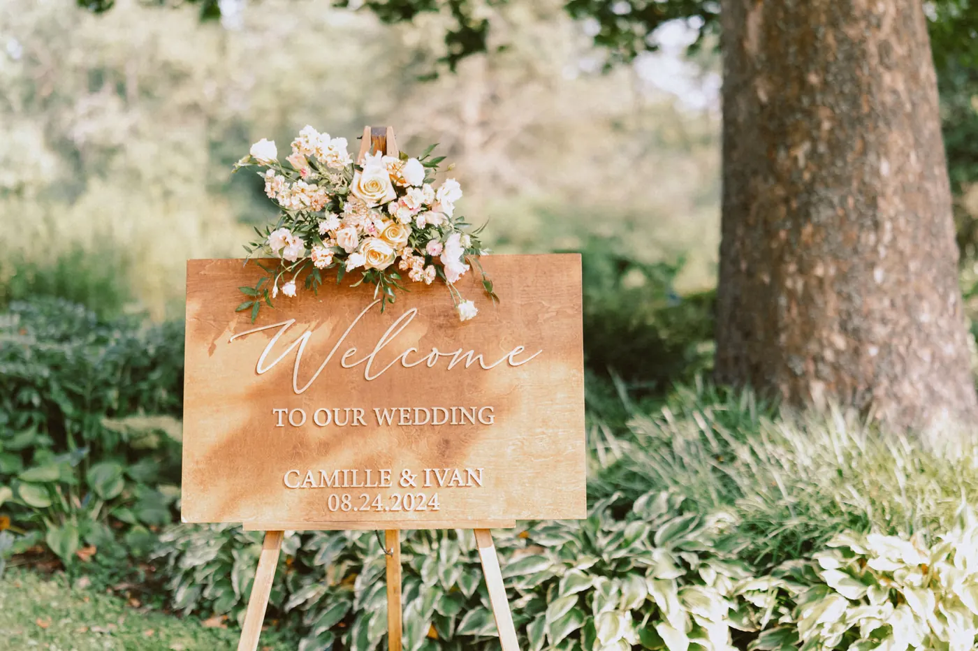 Wooden welcome sign topped with peach flowers for Camille and Ivan's wedding at Bishop Farmstead