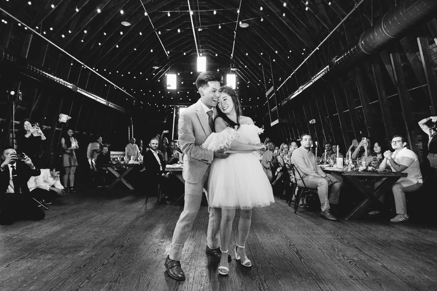 Black and white photo of Ivan and Camille slow dancing as guests watch