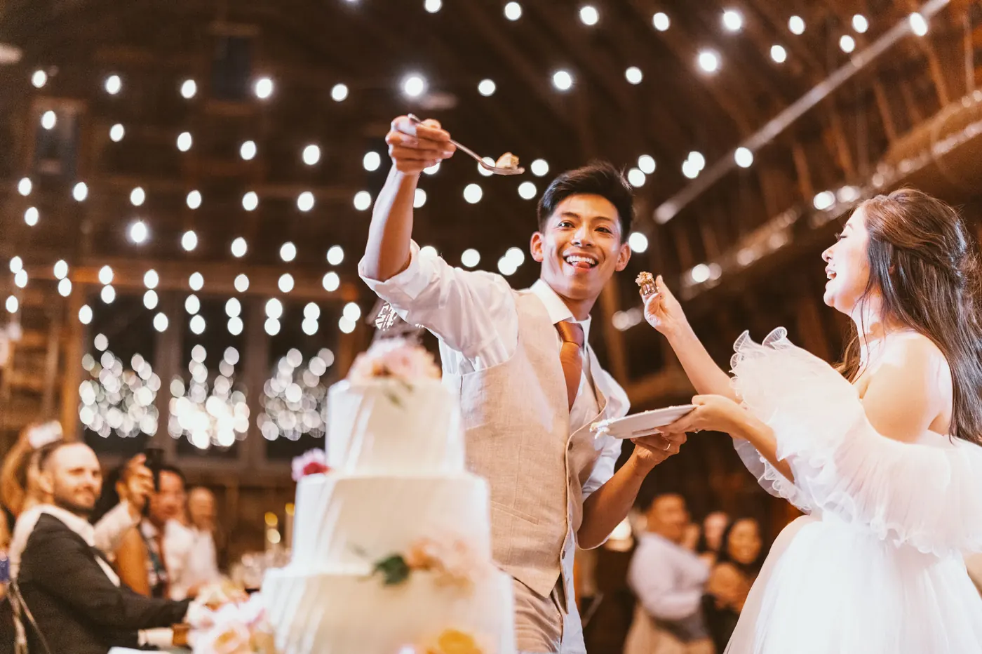 Ivan laughing as he holds up a piece of cake under the string lights