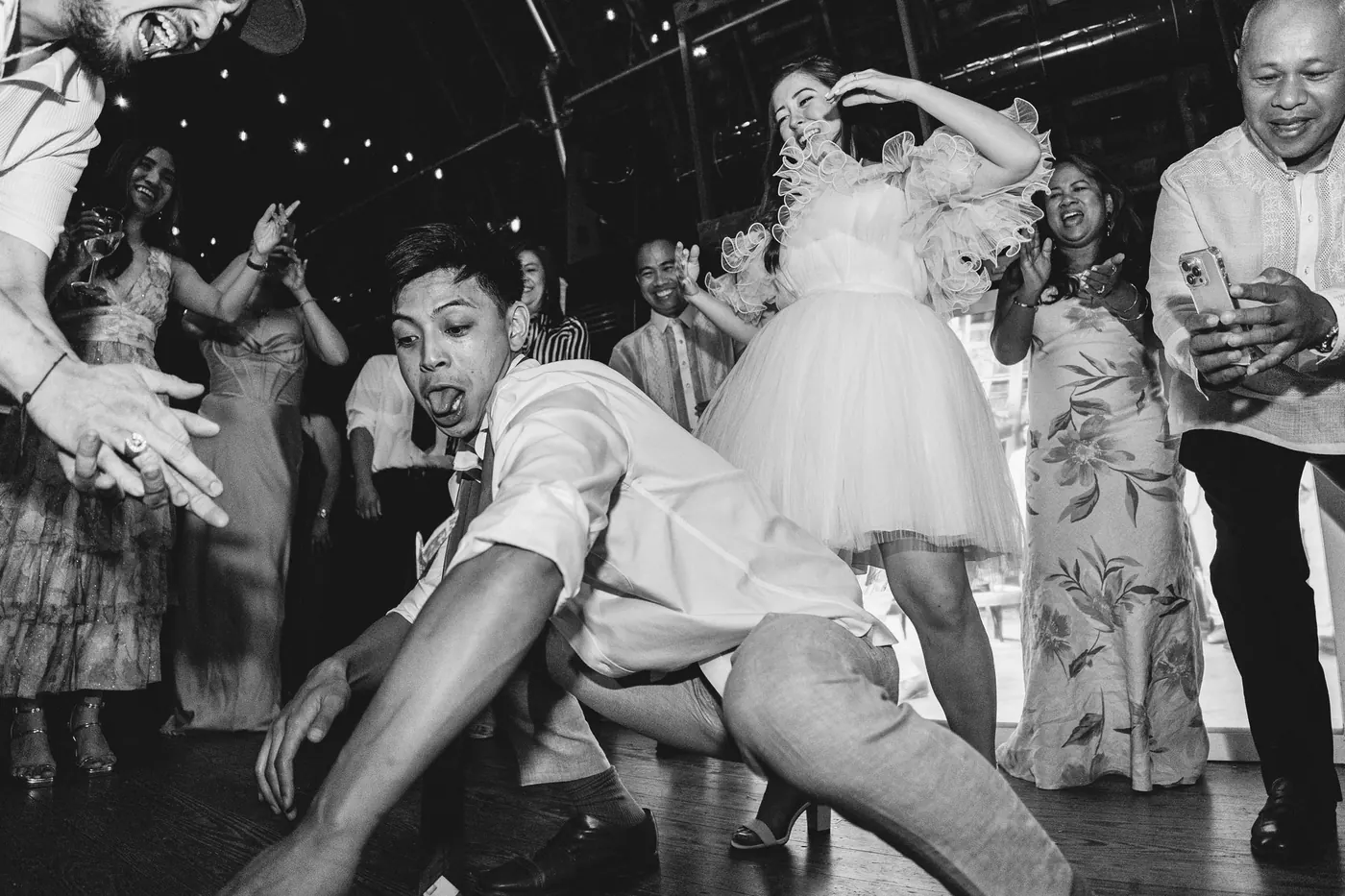 Black and white photo of Ivan dancing low as Camille and guests cheer