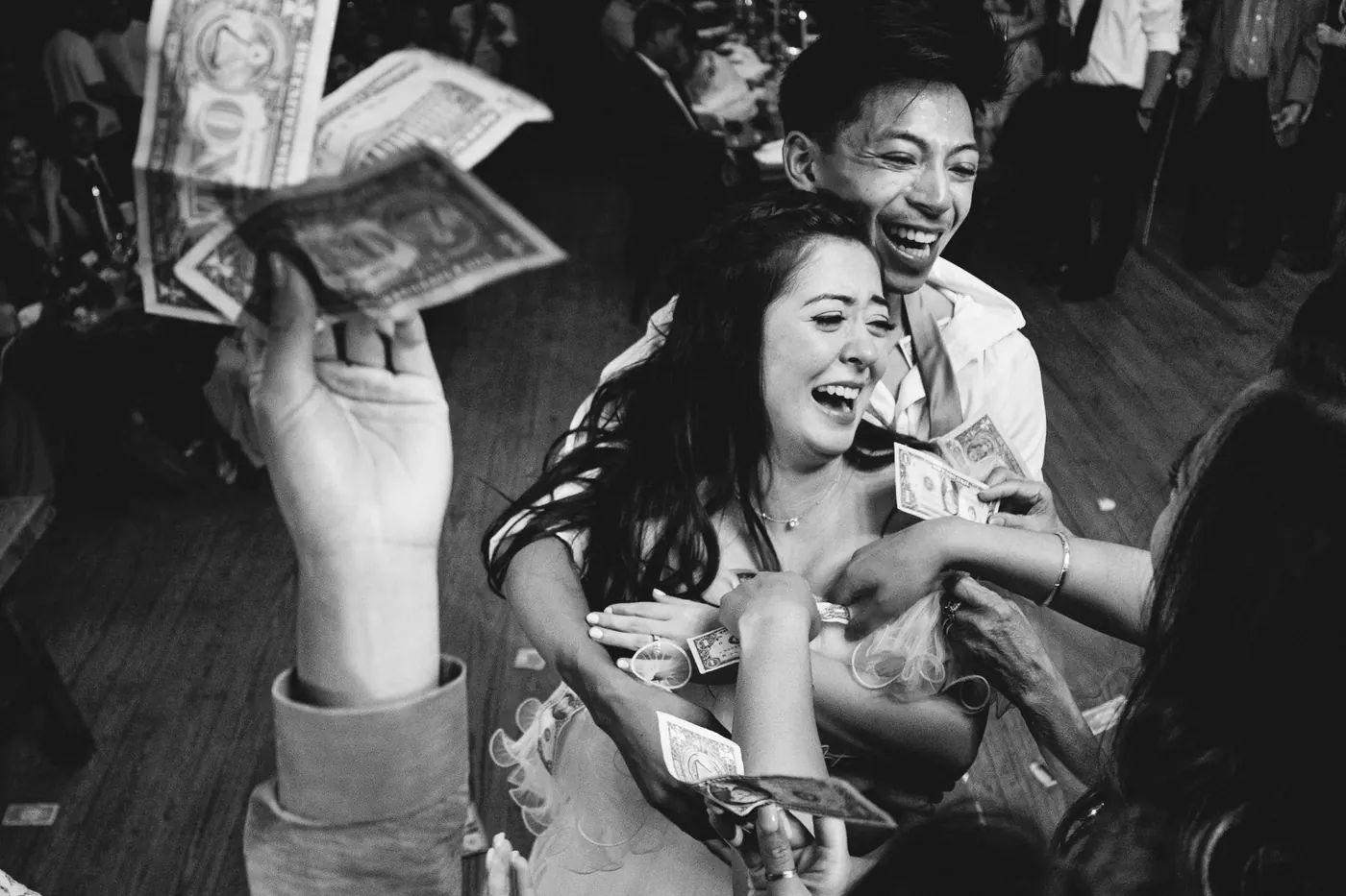 Black and white photo of Camille laughing as guests shower her with dollar bills