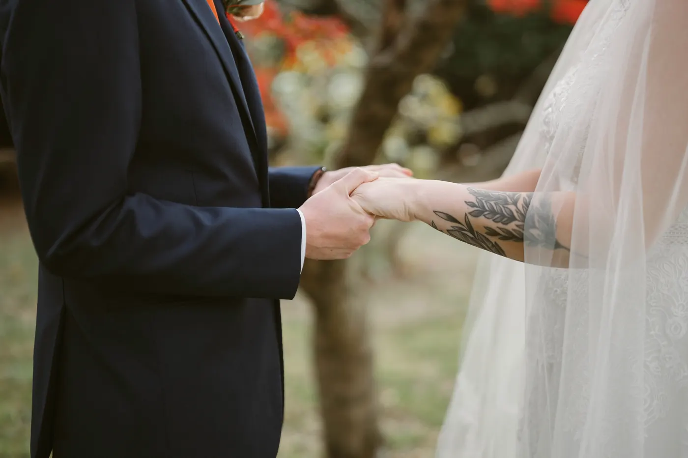 Close-up of Jimmy holding Kelsey's tattooed arm under the autumn trees