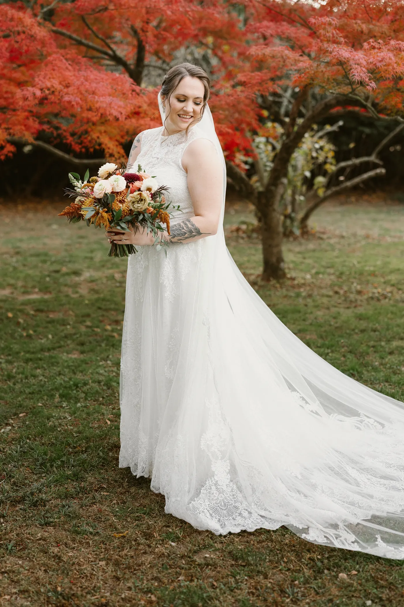 Kelsey holding her autumn bouquet in front of the red maple
