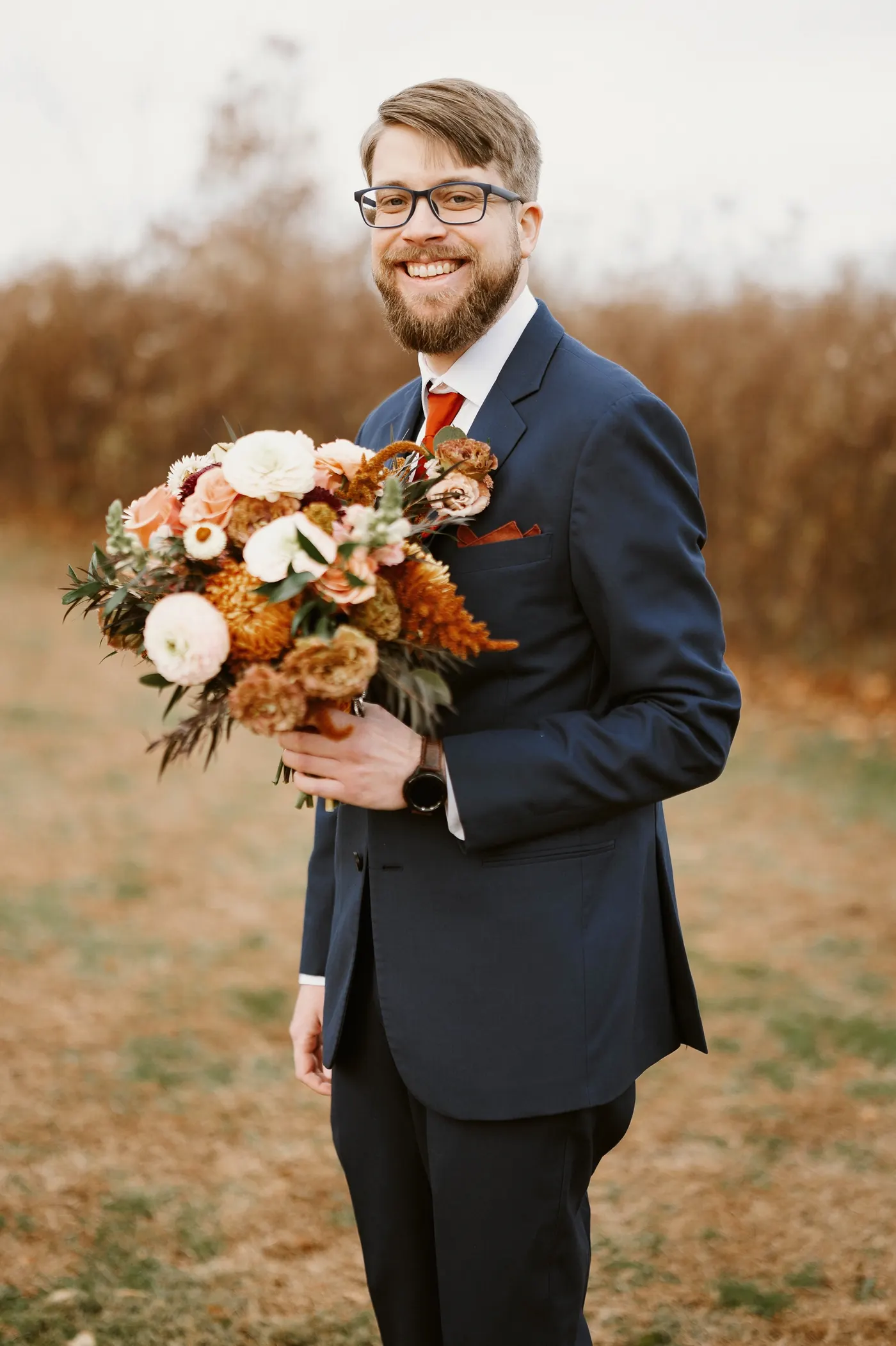 Jimmy smiling as he holds Kelsey's bouquet in the tall autumn grass
