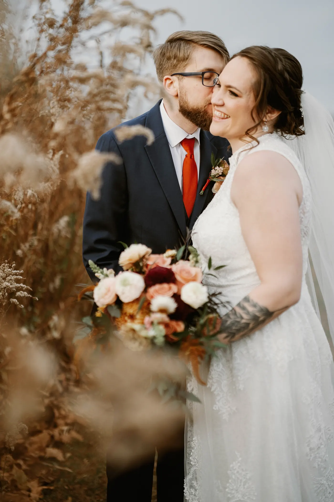Jimmy kissing Kelsey on the cheek as she holds her bouquet in the meadow