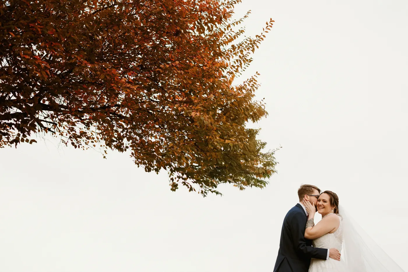 Jimmy and Kelsey kissing beneath a canopy of orange autumn leaves