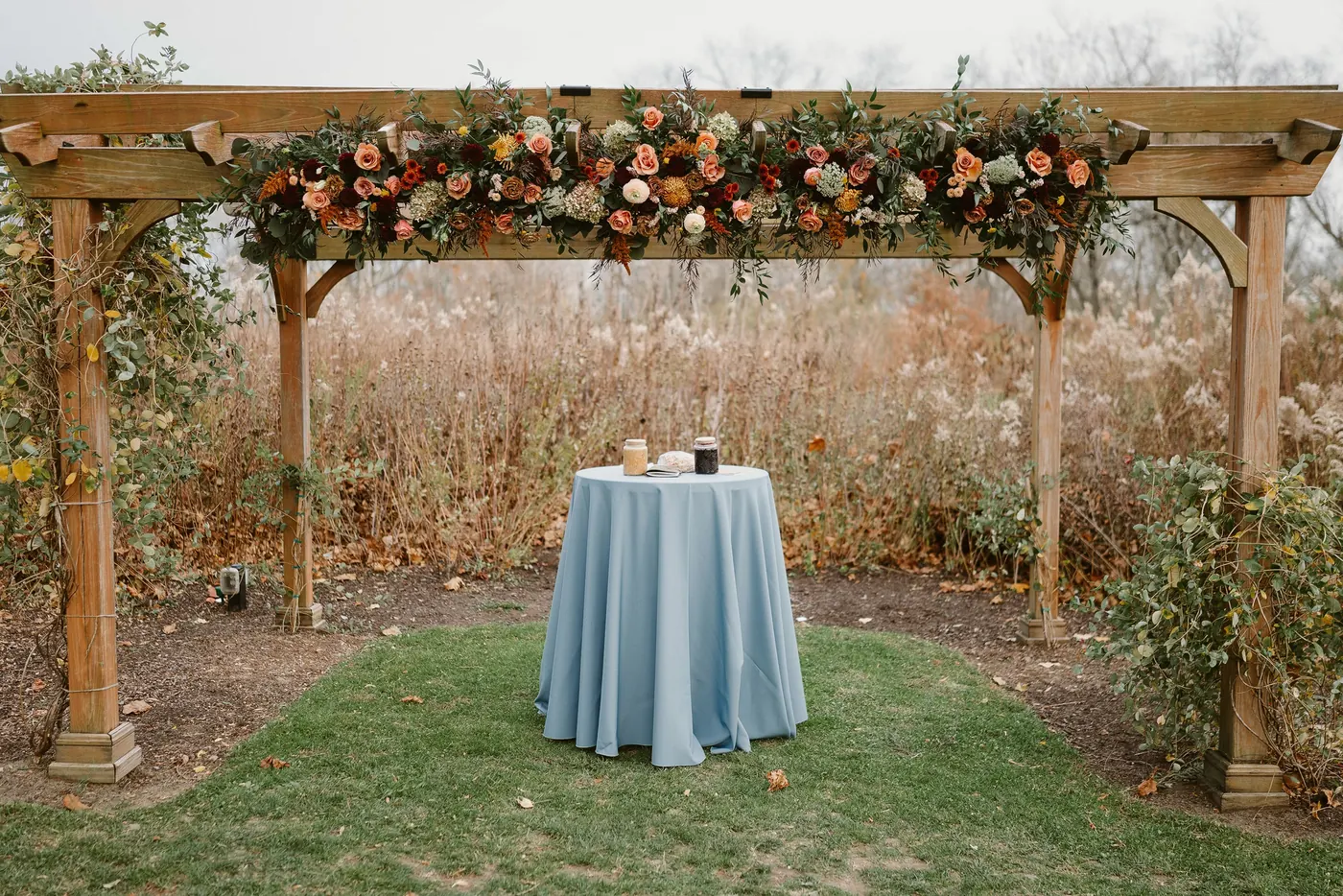 The wooden pergola draped in autumn flowers with the ceremony table set beneath it