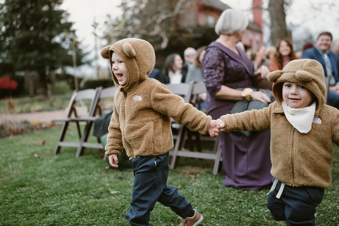 Two little kids in fuzzy bear jackets running down the aisle hand in hand