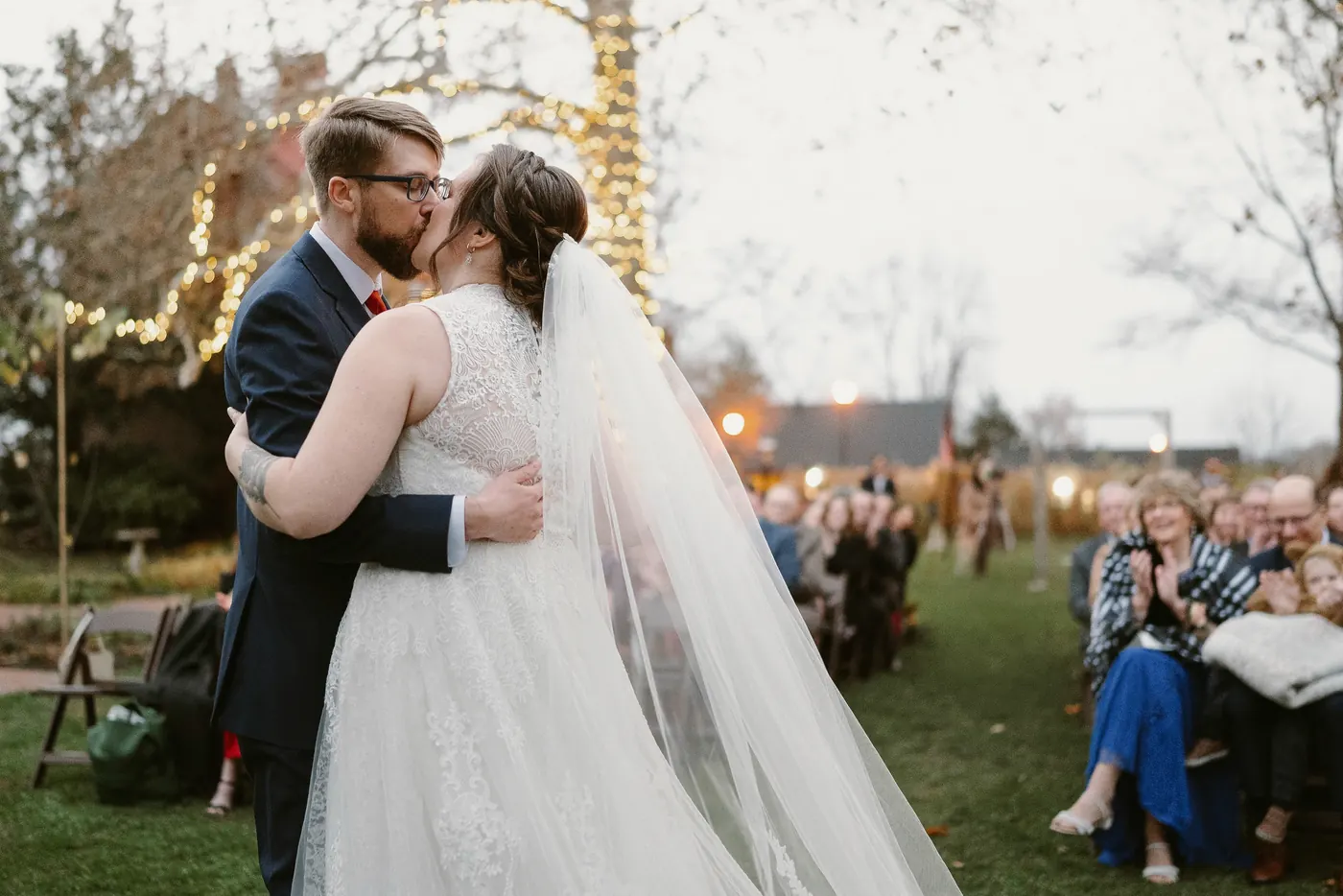 Jimmy and Kelsey's first kiss as guests cheer under the string lights
