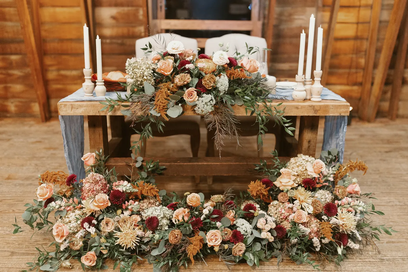 The sweetheart table in the barn covered in autumn flowers and candles