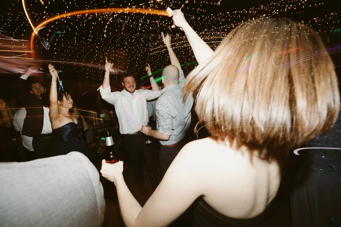 Guests dancing with hands up under swirling string lights in the barn
