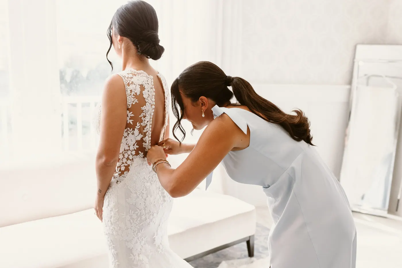 A bridesmaid buttoning the back of Morgan's lace wedding gown